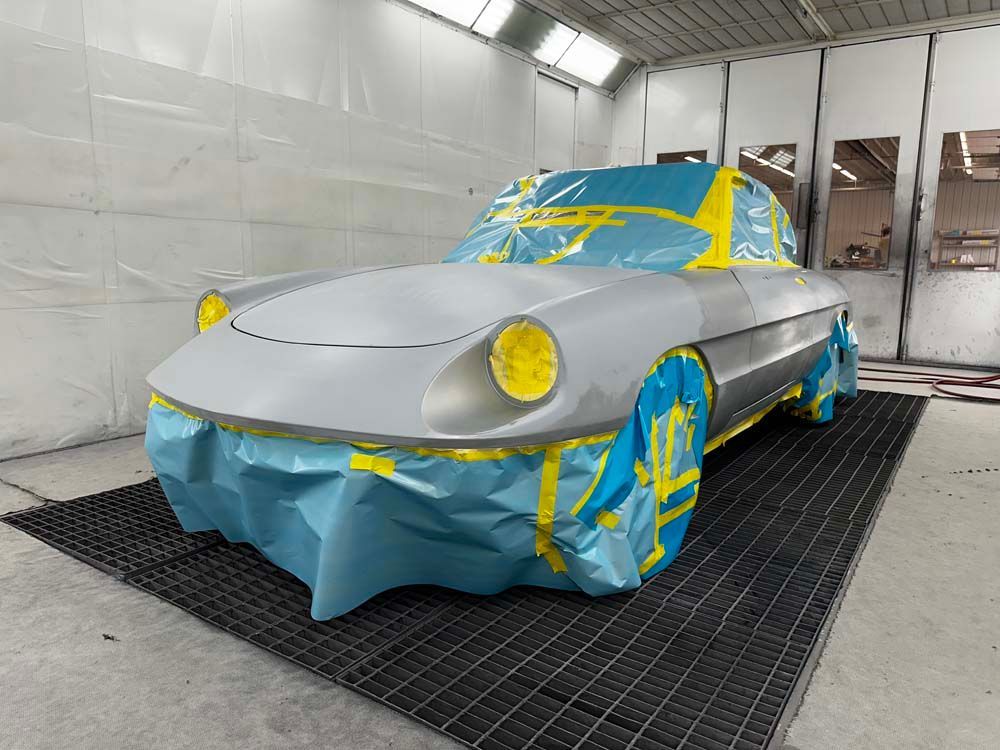 A car is covered in blue and yellow tape in a paint booth.