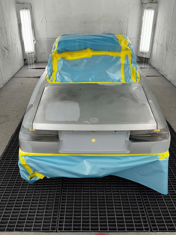 A car is covered in blue and yellow tape in a paint booth.