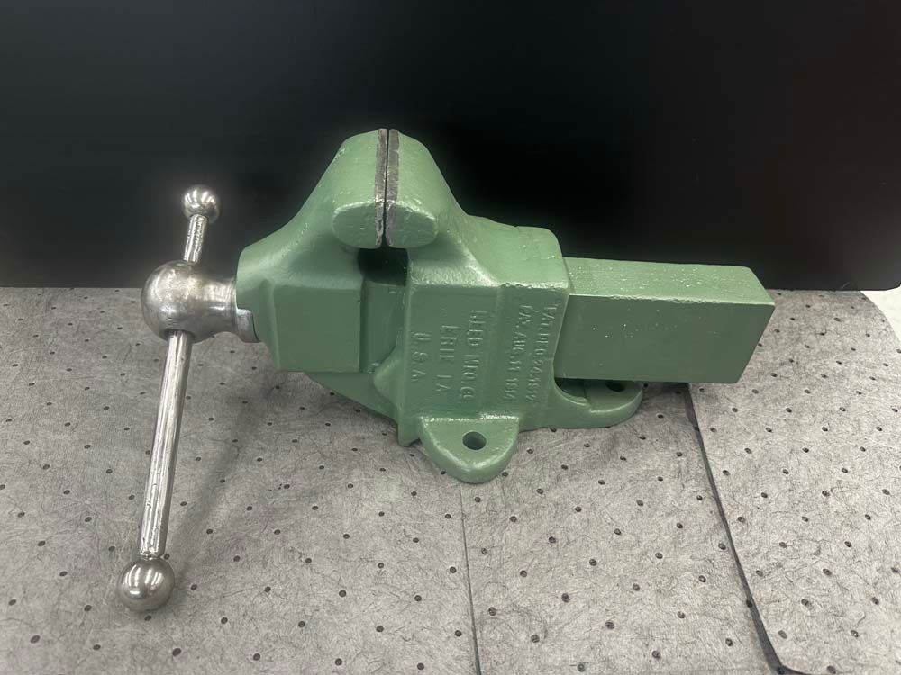 A green vise with a handle is sitting on a table.