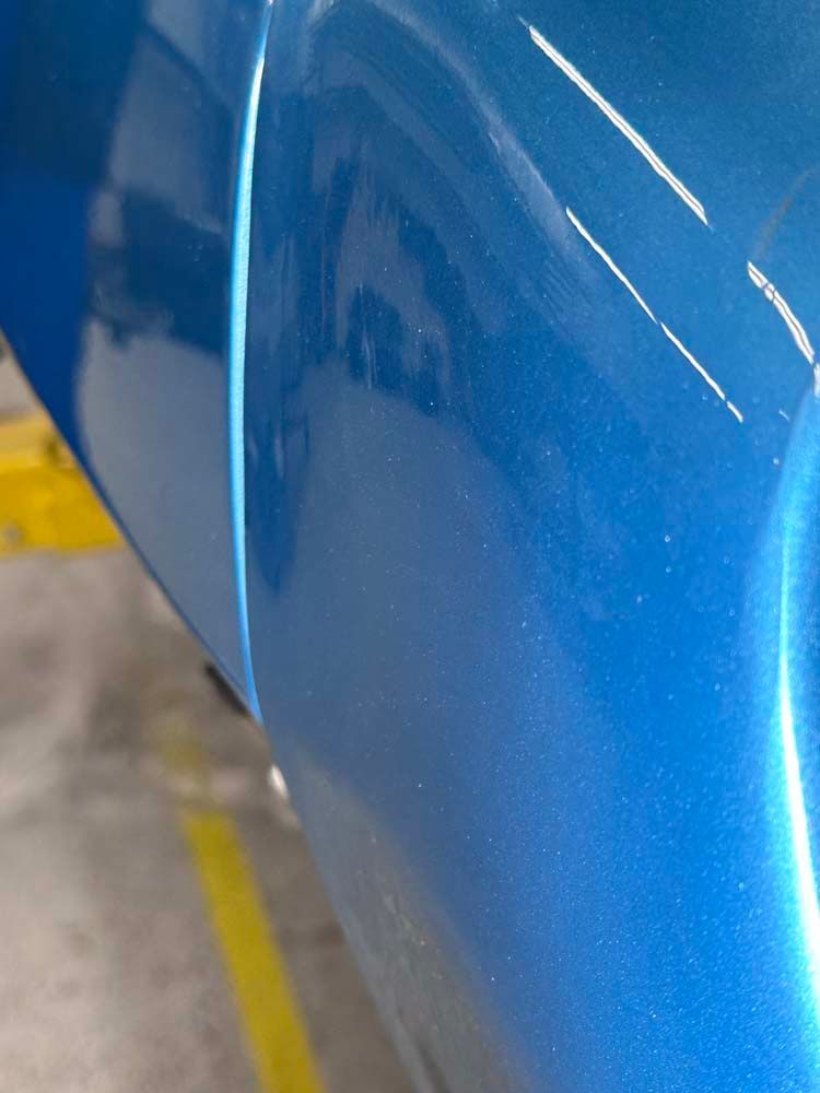 A close up of a blue car with a yellow line in the background.