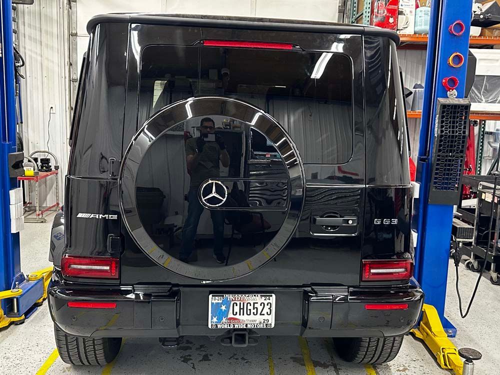 A black mercedes benz g63 amg is parked on a lift in a garage.