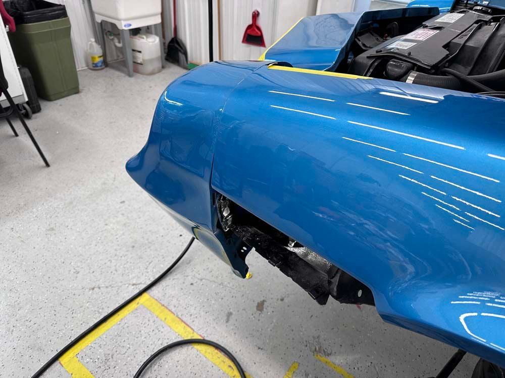 A blue car is sitting in a garage with the hood open.