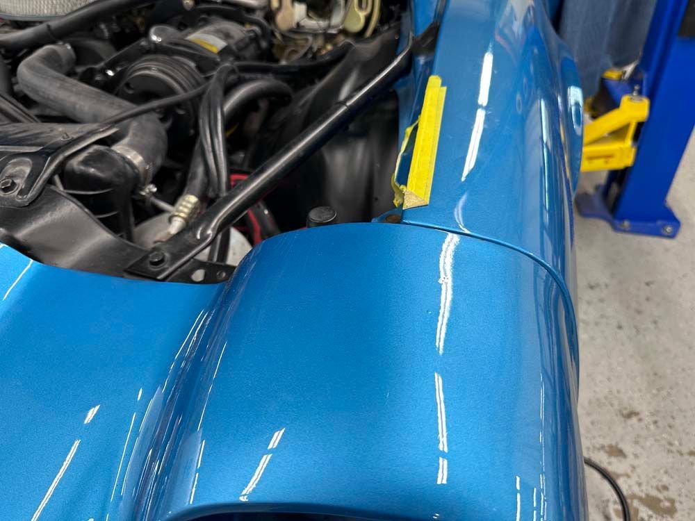 A blue car with a yellow stripe on the fender
