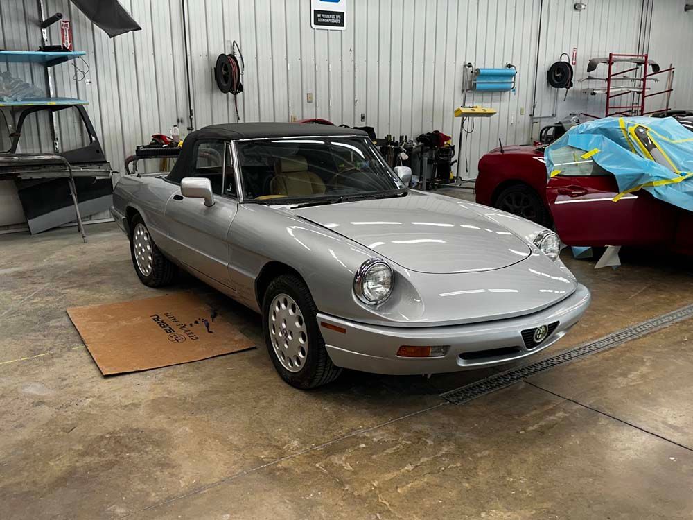 A silver car is parked in a garage next to a red car.