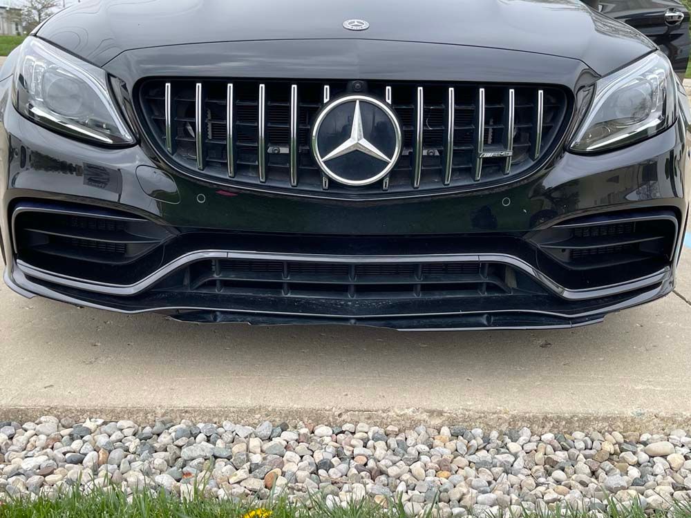 The front of a black mercedes benz is parked in a driveway.