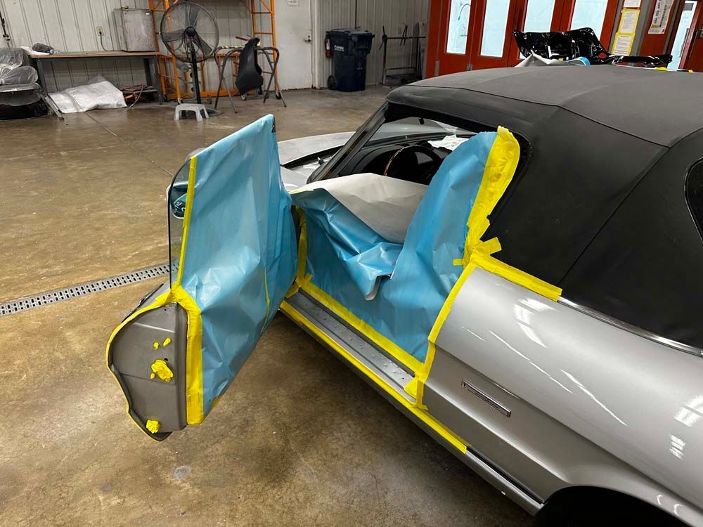 A silver car is being painted in a garage.