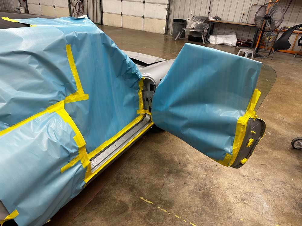 A car is wrapped in blue plastic and yellow tape in a garage.