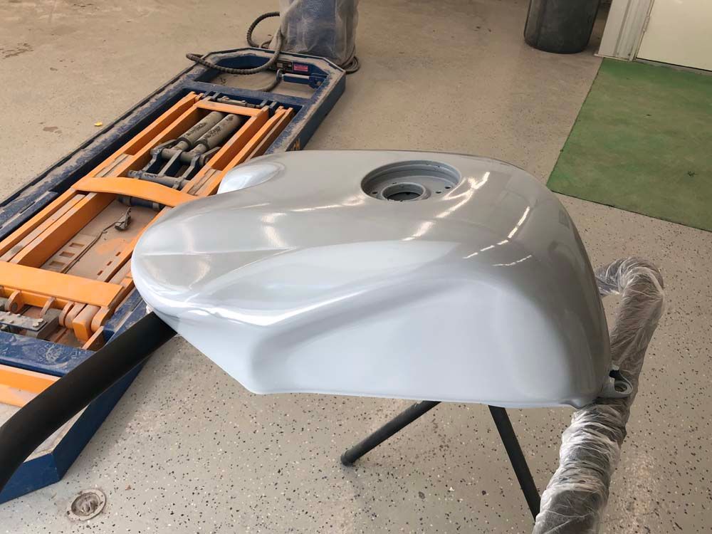 A white motorcycle tank is sitting on a stand next to a lift.