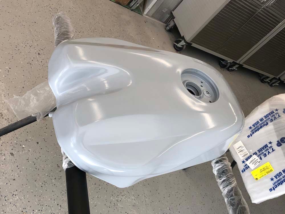 A white motorcycle tank is sitting on a stand in a garage.