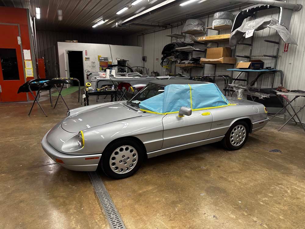 A silver sports car is parked in a garage with a blue tarp on the windshield.