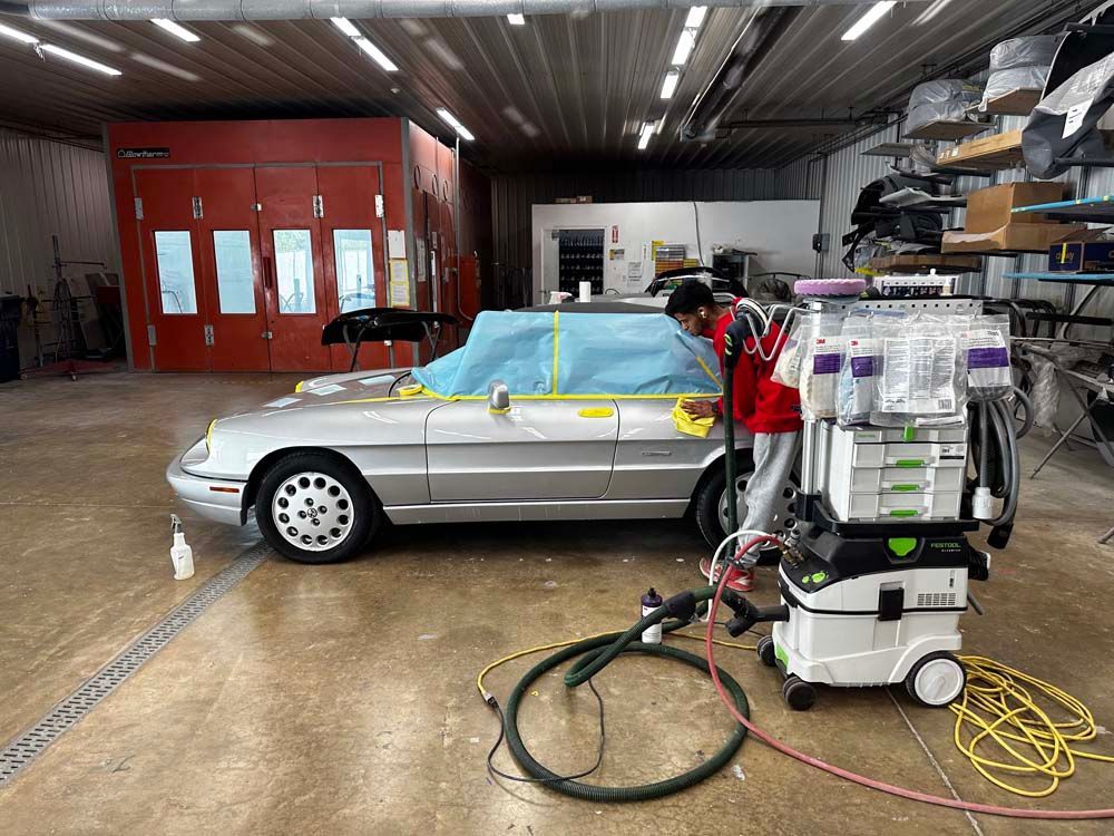 A man is polishing a silver car in a garage.