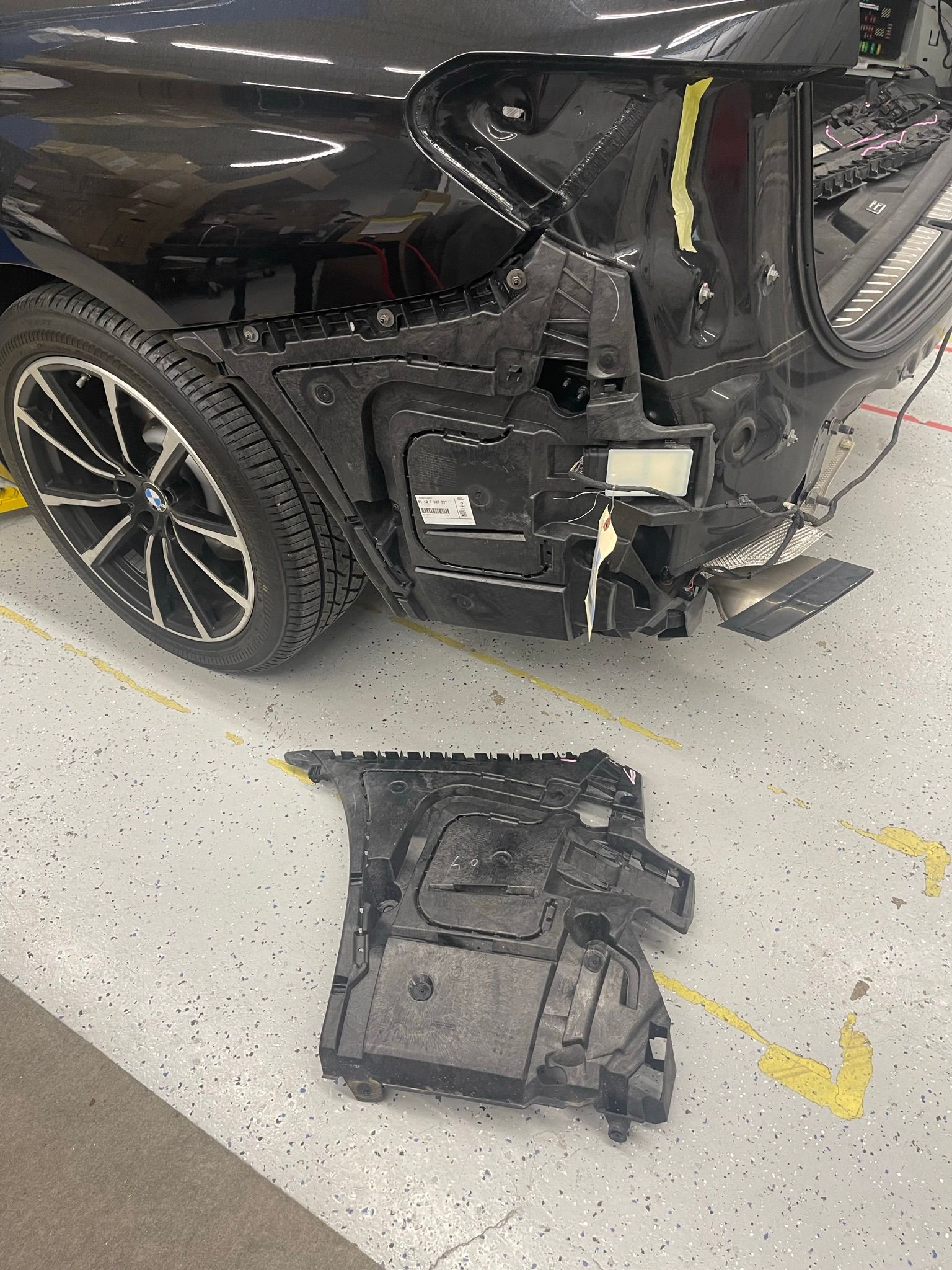 A black car with a damaged bumper is sitting in a garage.
