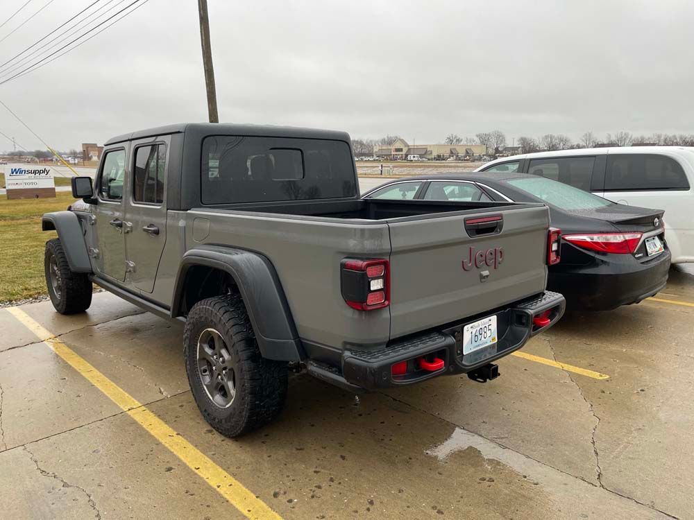 A jeep gladiator is parked next to a black car in a parking lot.