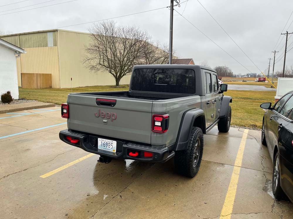 A jeep gladiator is parked in a parking lot next to a black car.