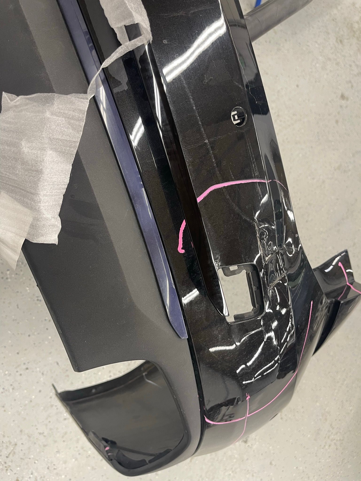 A black car bumper is sitting on a white floor.