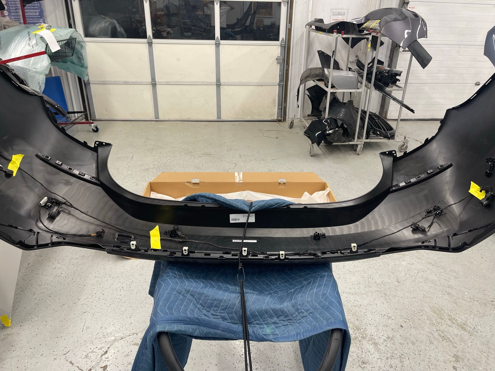 A car bumper is sitting on a blue blanket in a garage.