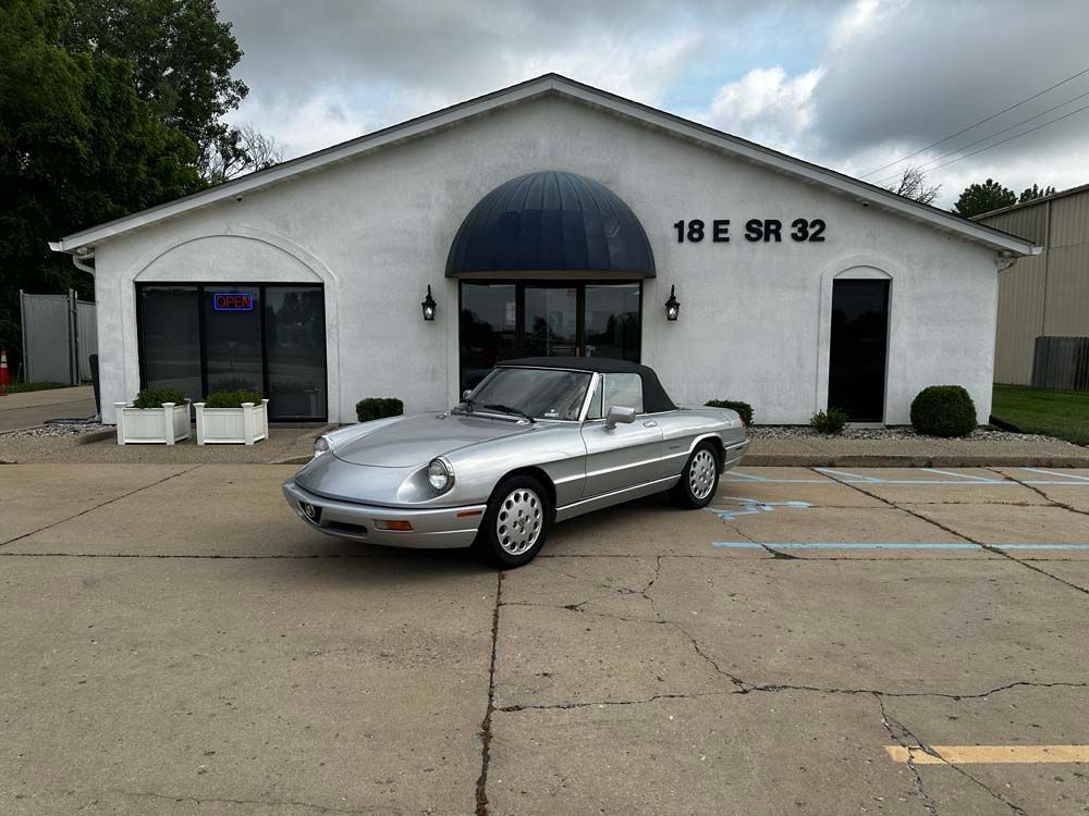 A silver car is parked in front of a white building.