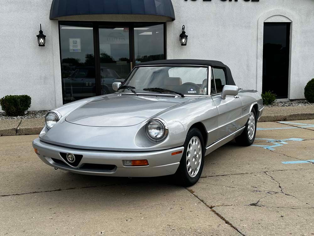 A silver convertible is parked in front of a building.