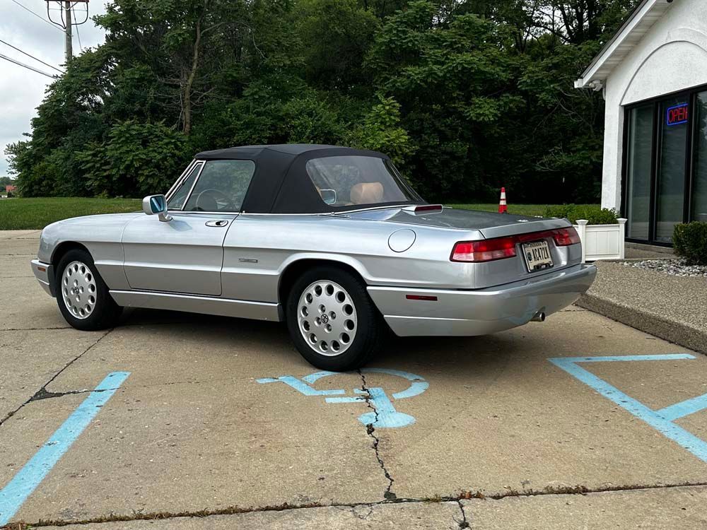 A silver convertible is parked in a handicapped parking spot