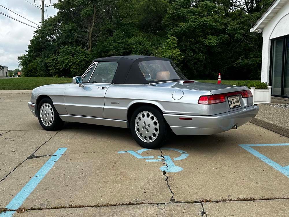 A silver convertible is parked in a handicapped parking spot
