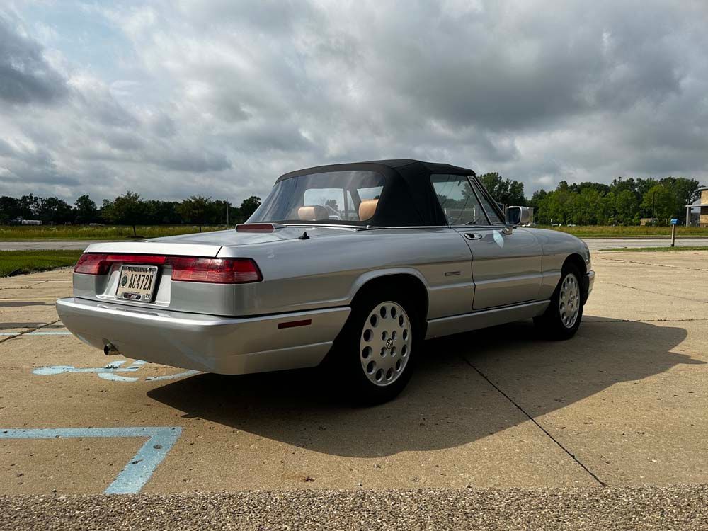 A silver convertible car is parked in a parking lot