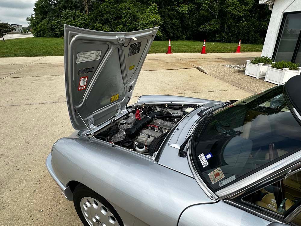 A silver car with the hood up is parked in a parking lot.