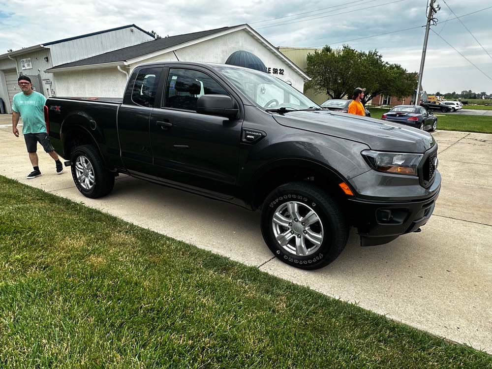 A man is standing next to a black truck parked on the side of the road.