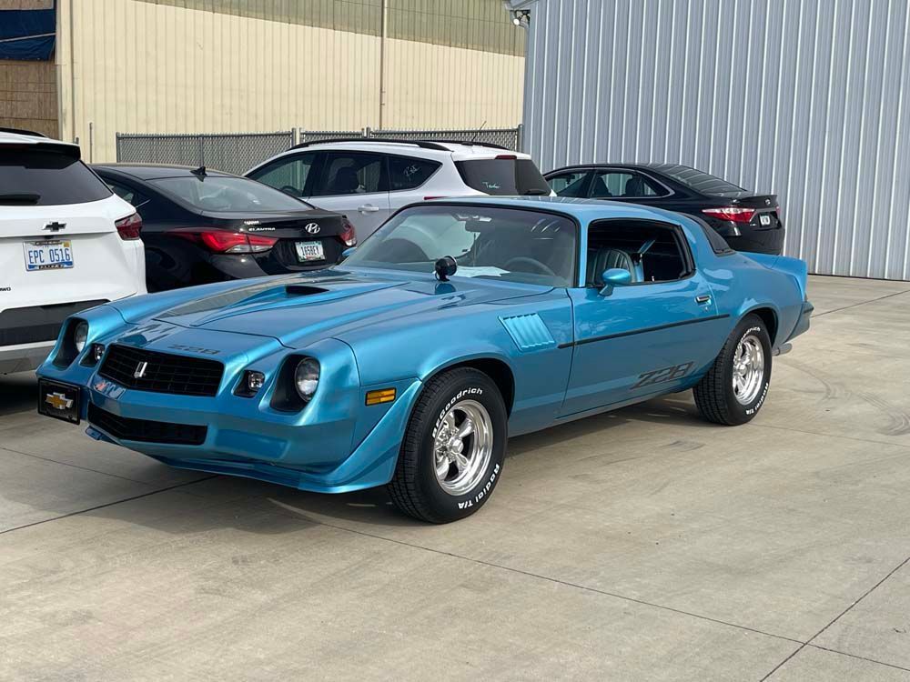 A blue car is parked in a parking lot next to other cars.