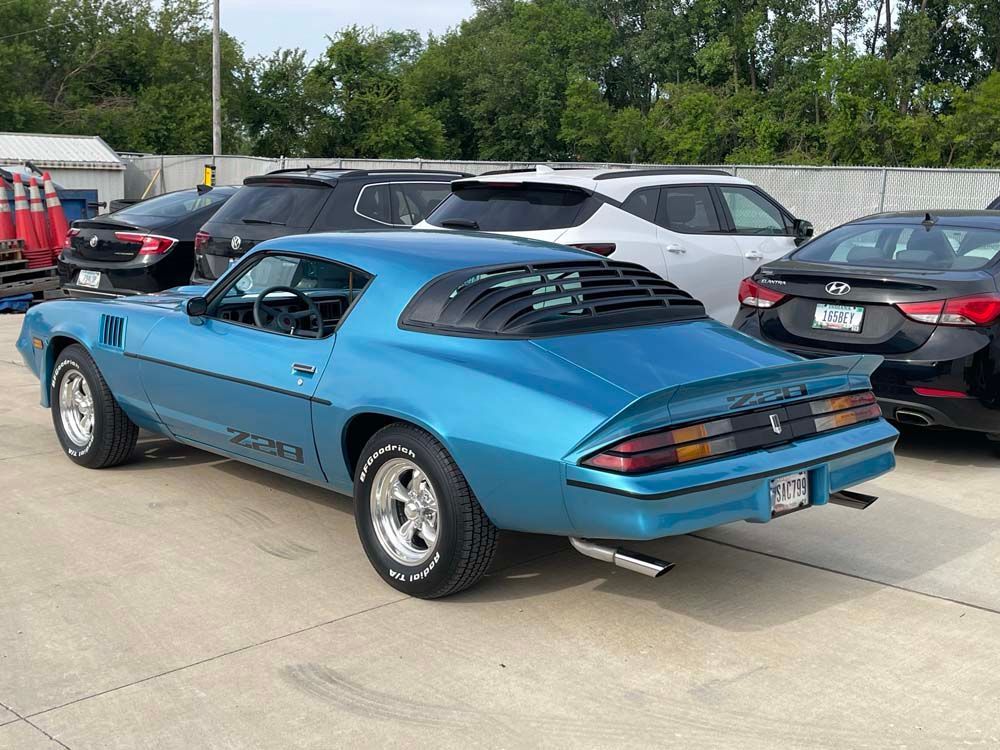 A blue car is parked in a parking lot next to other cars.