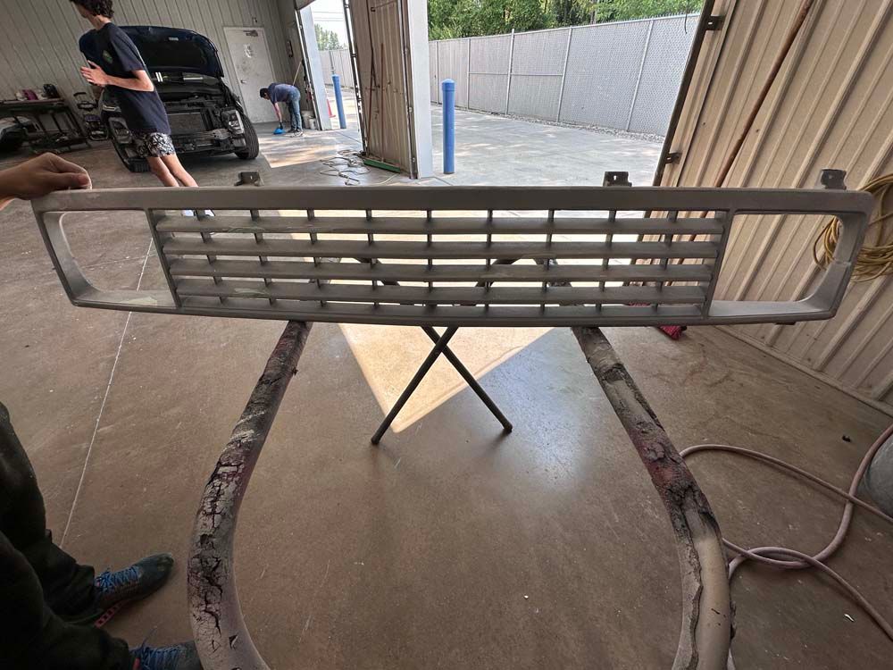 A person is holding a front grill in a garage.