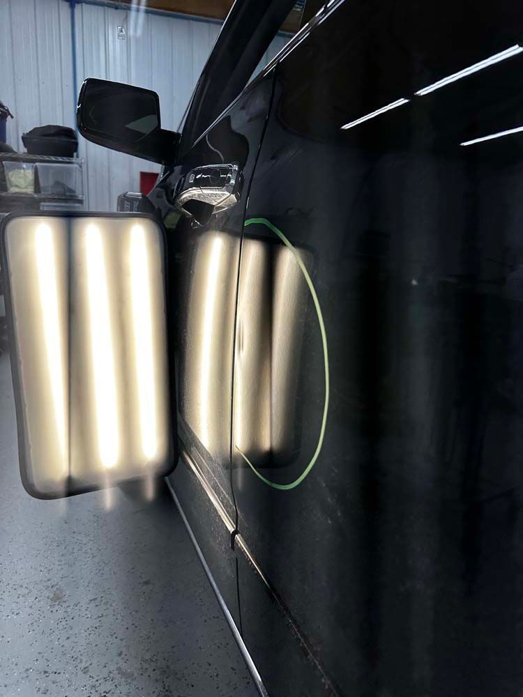 A black car is sitting in a garage with a green circle around it.