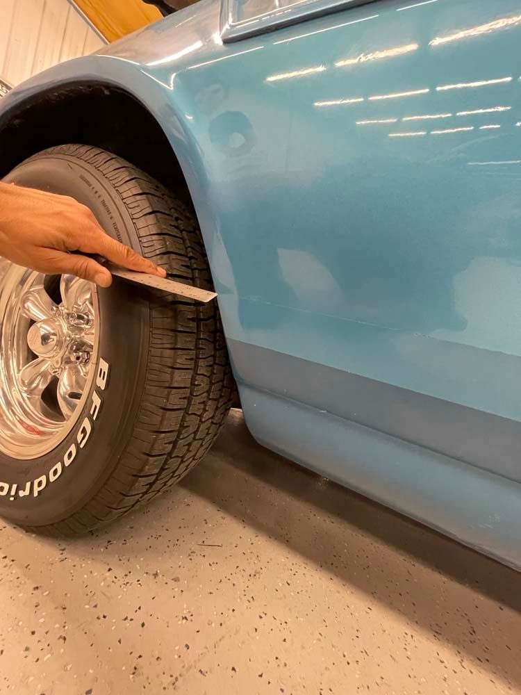 A person is holding a piece of paper over a tire on a blue car.