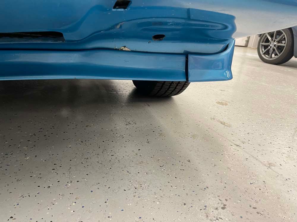 A blue car is parked in a garage with a damaged bumper.