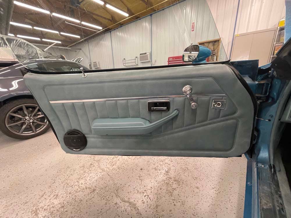 The door of a blue car is open in a garage.