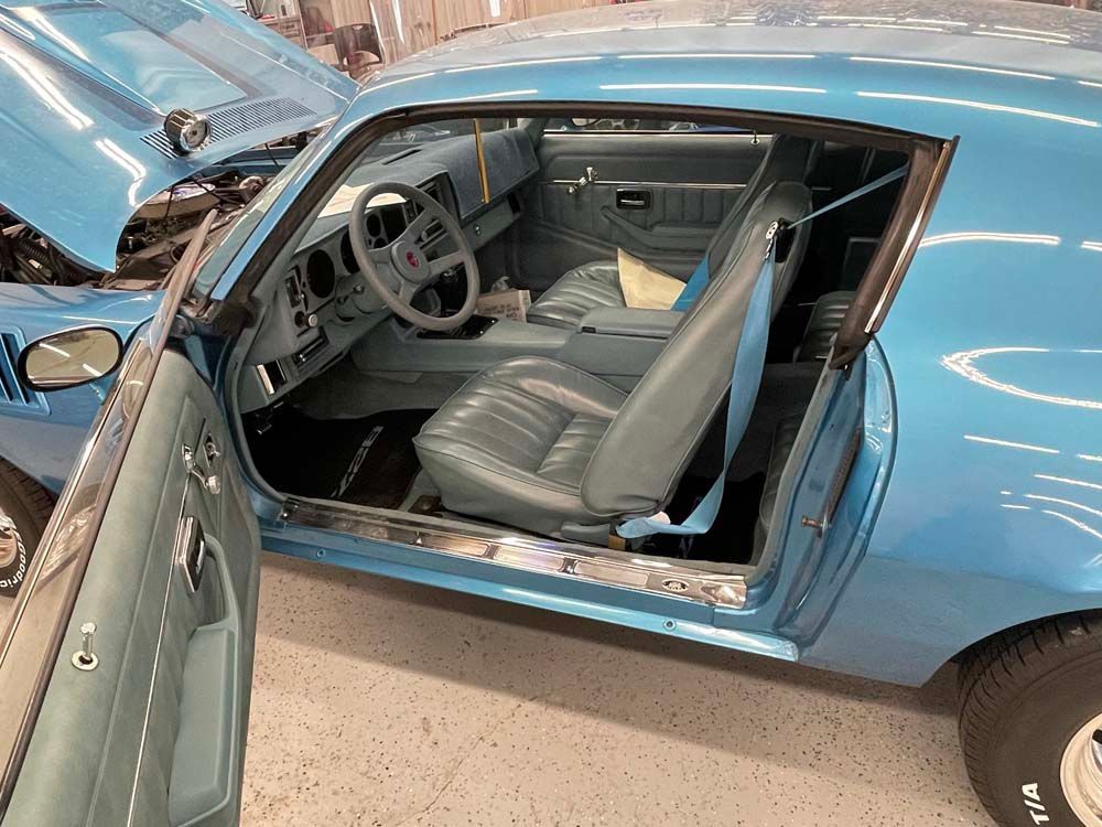 A blue car with the door open is parked in a garage.