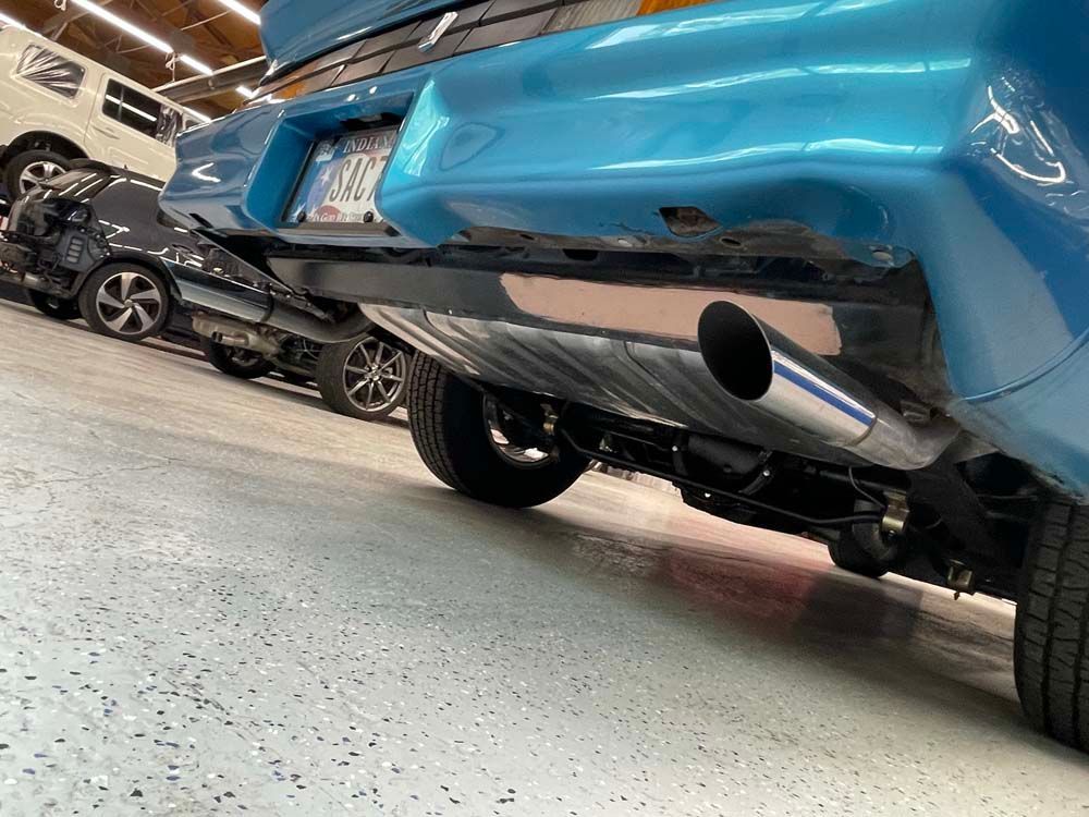 A blue car with a stainless steel exhaust pipe is parked in a garage.