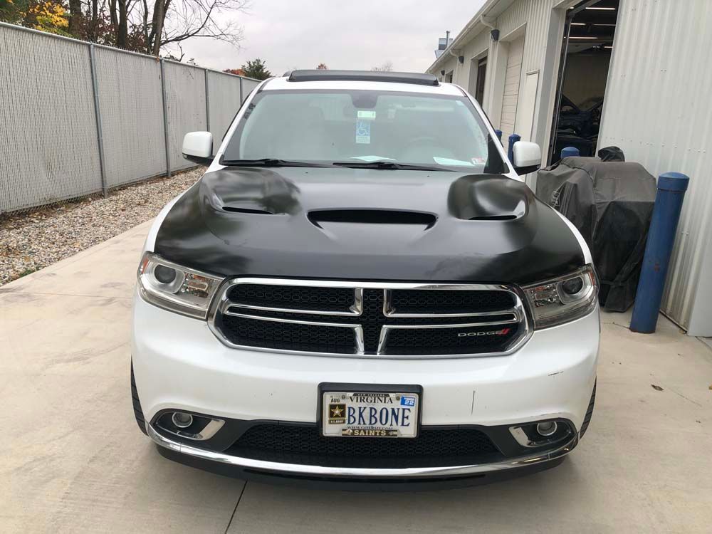 A white dodge durango with a black hood is parked in a driveway.