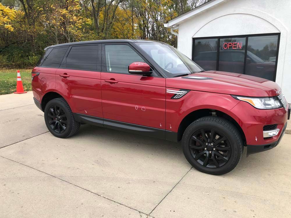 A red range rover sport is parked in a driveway in front of a garage.