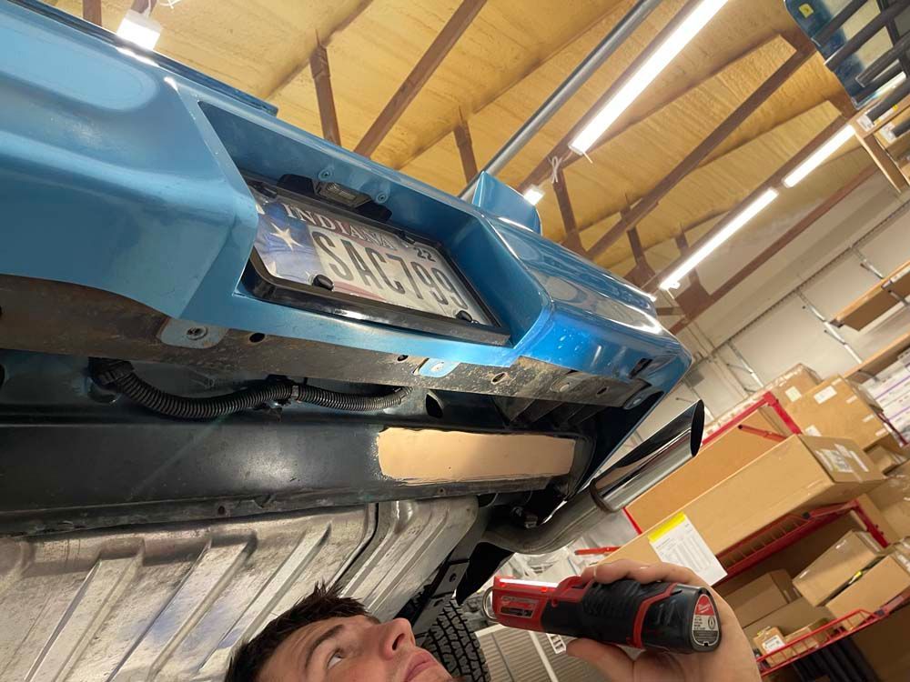 A man is using a drill to remove a license plate from a car.