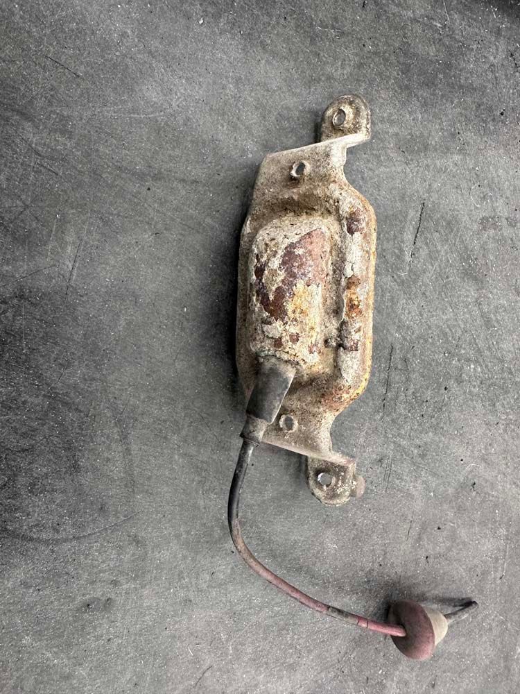 A piece of metal with a wire attached to it is sitting on a concrete surface.