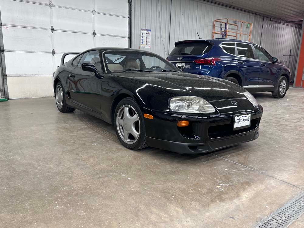 A black toyota supra is parked in a garage next to a blue suv.