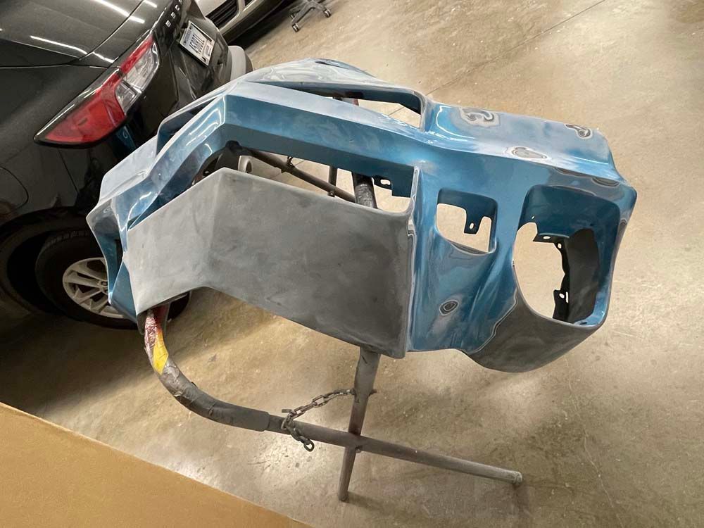 A car bumper is sitting on a stand in a garage next to a car.