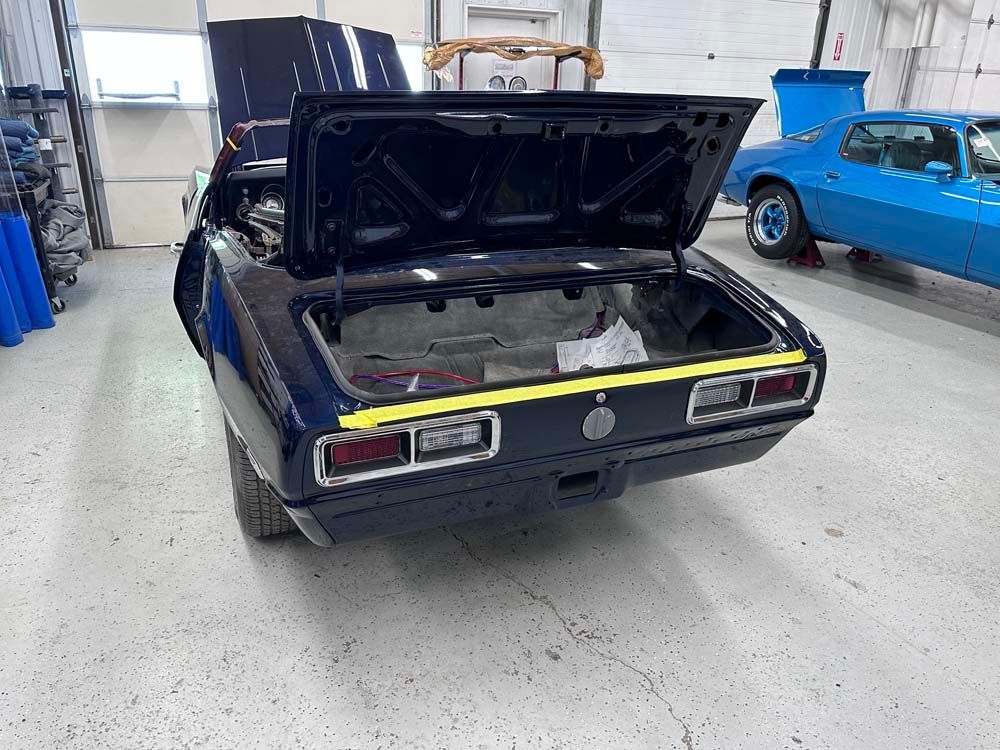 A blue car is parked in a garage with the trunk open.