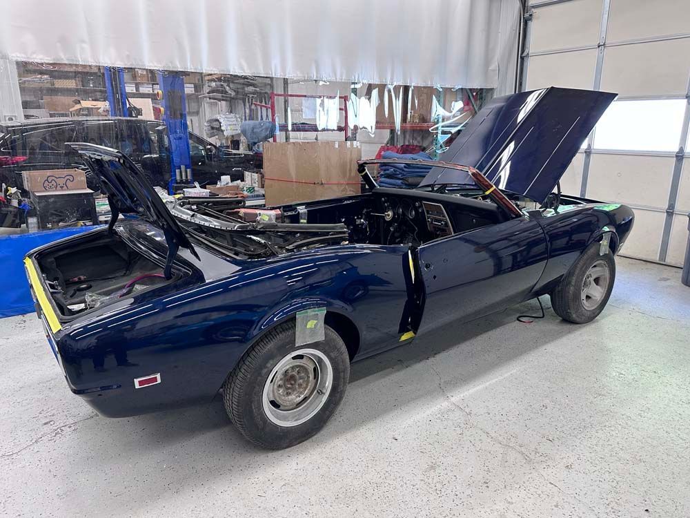 A blue convertible car with the hood up is sitting in a garage.