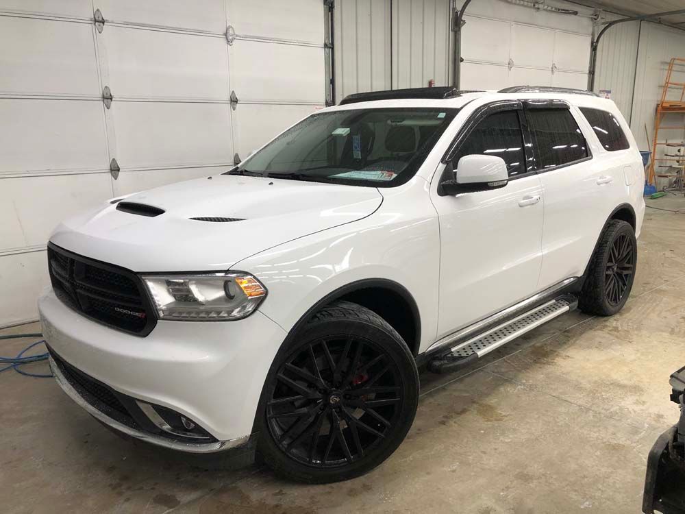 A white dodge durango is parked in front of a garage door.