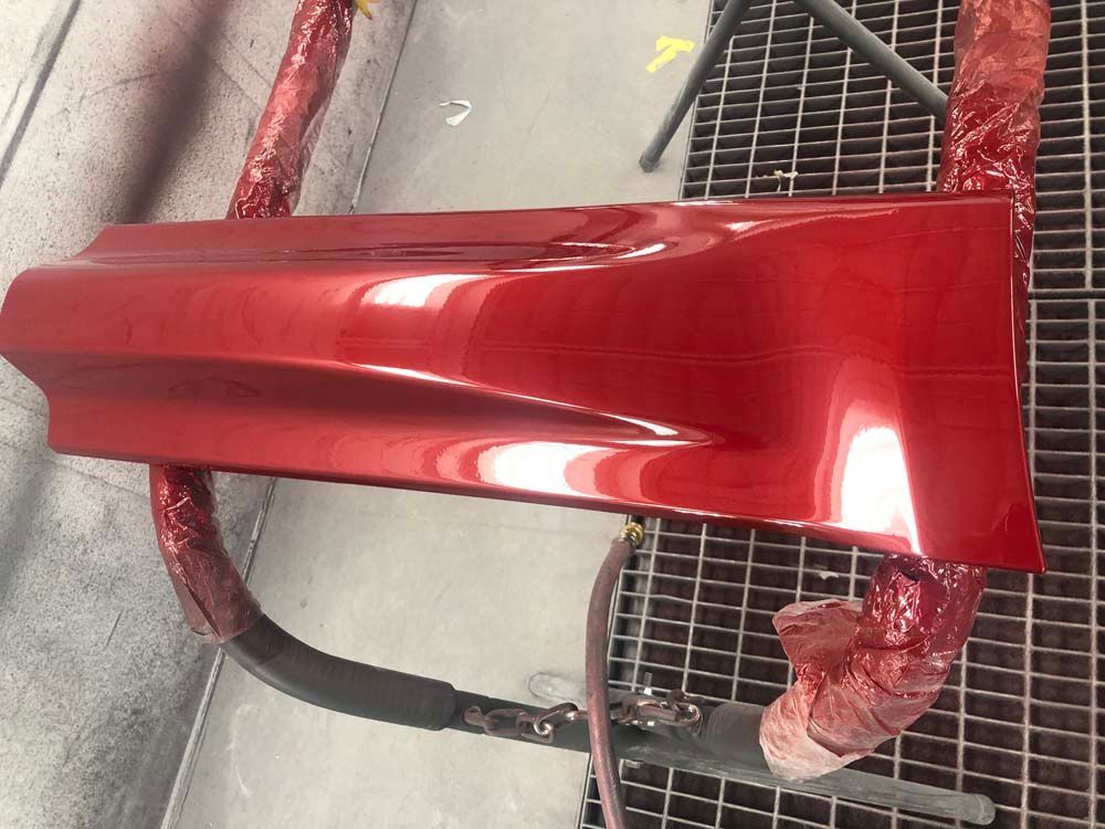 A red car is being painted in a paint booth.