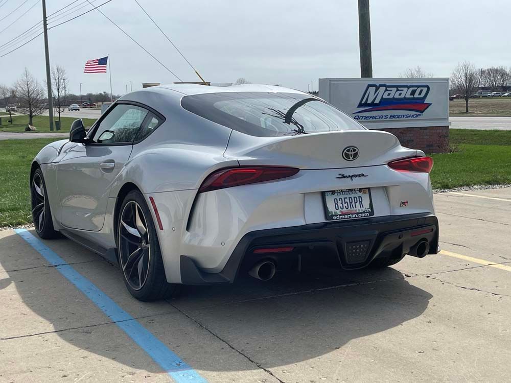 A silver sports car is parked in a parking lot in front of a maasco sign.
