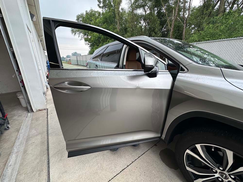 A silver car is parked in a garage with its door open.