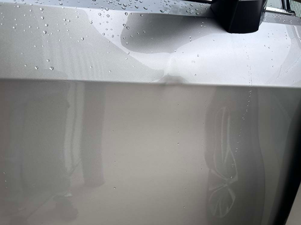 A close up of a car 's hood with water drops on it.