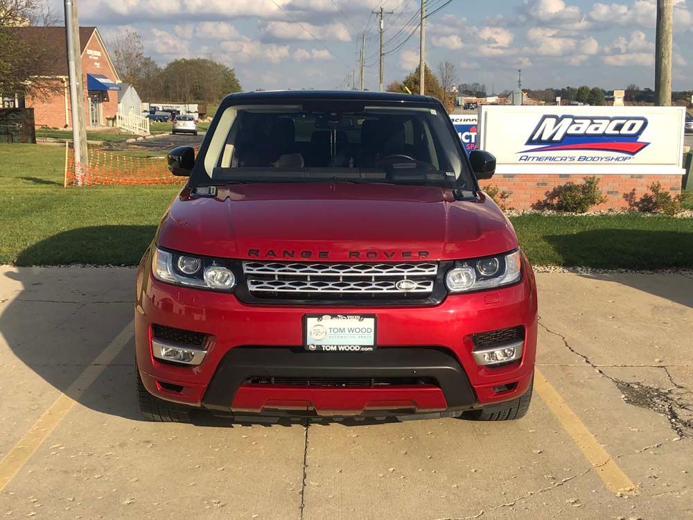 A red range rover sport is parked in a parking lot in front of a maaco sign.